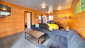 A modern living room with wooden walls, a grey sofa, a wooden coffee table, and a flat-screen TV. - Wellington TOP 10 Holiday Park (Lower Hutt)