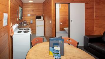 Une cuisine compacte équipée d’une cuisinière, d’un four à micro-ondes et d’un évier. On y trouve une table à manger avec une brochure et une télécommande. Un canapé en cuir noir se trouve dans l’espace salon.