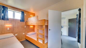Une chambre avec un lit superposé, une tête de lit en bois, une porte blanche et une fenêtre avec des rideaux.