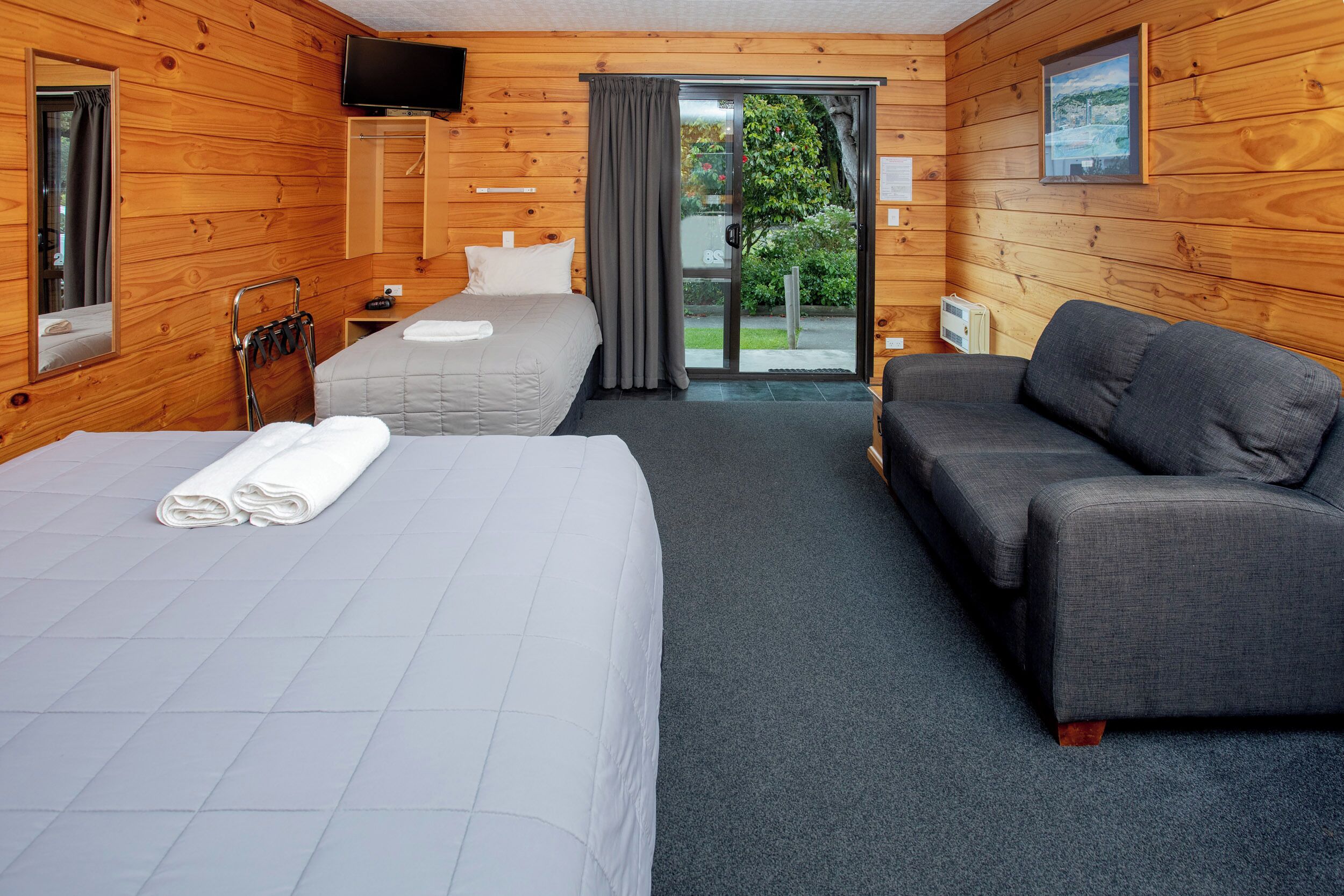 Habitación con dos camas, un sofá, un televisor y un ventanal corredizo al exterior.