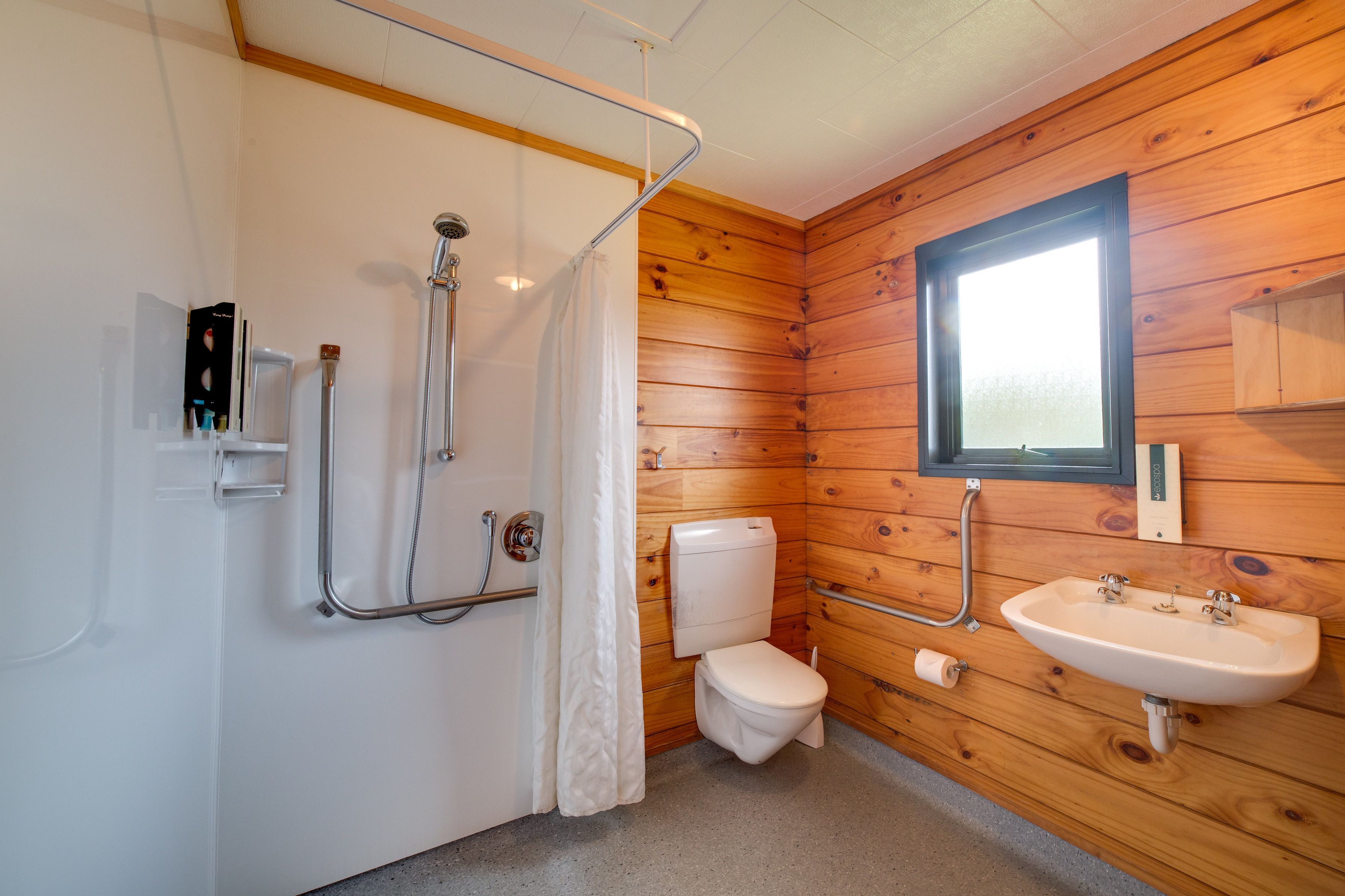Une salle de bain aux murs lambrissés, équipée d’une douche, de toilettes et d’un lavabo.