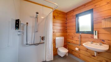Une salle de bain aux murs lambrissés, équipée d’une douche, de toilettes et d’un lavabo.
