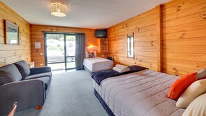 A cozy room with wooden walls, a bed with pillows, a sofa, and a television. - Wellington TOP 10 Holiday Park (Lower Hutt)