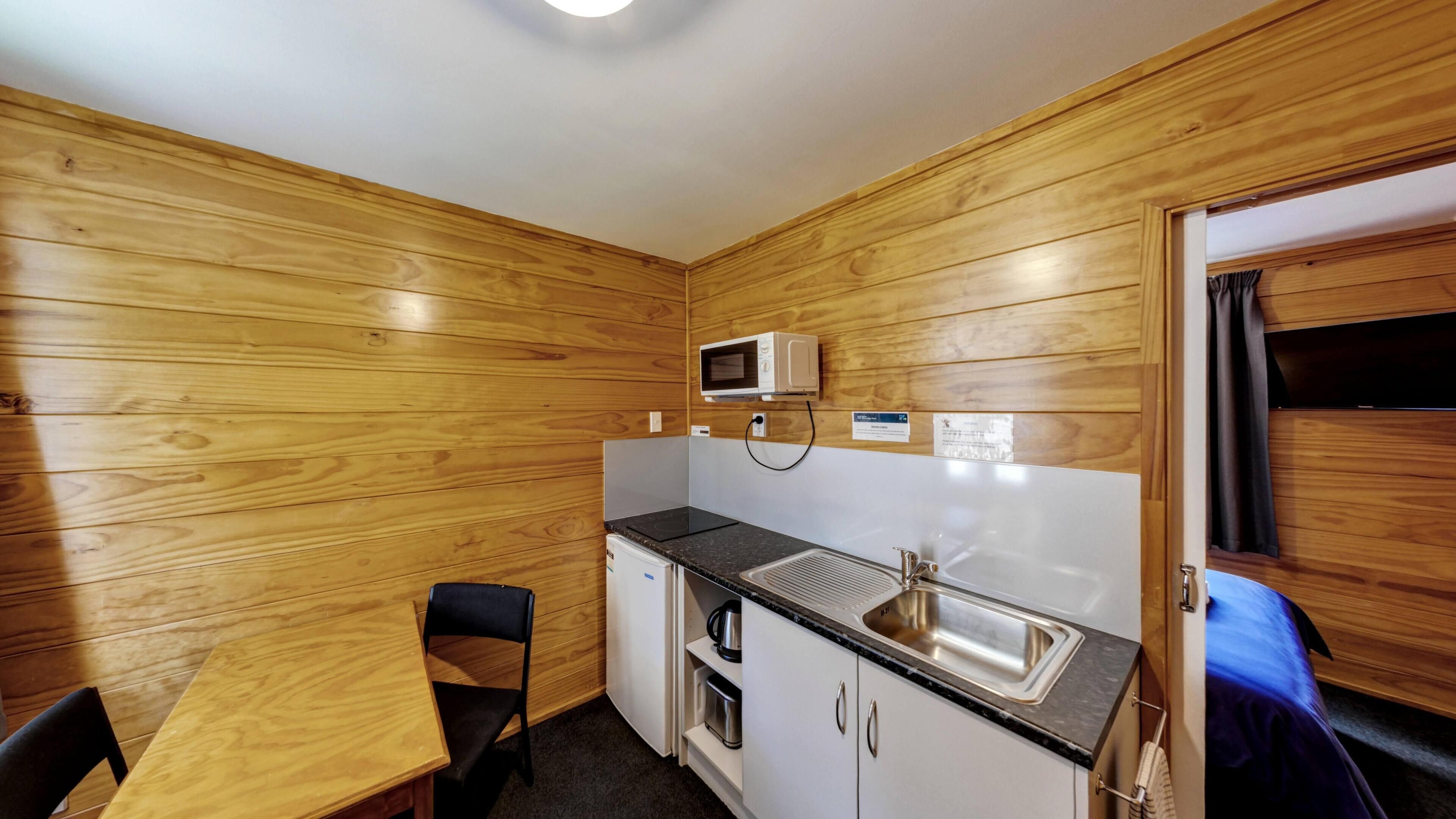 Una kitchenette compacta con microondas, pileta y un pequeño armario.