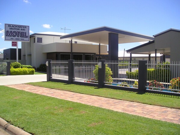 Un motel con área de estacionamiento techada, jardín cercado e indicación de sala de televisión.