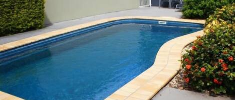 A swimming pool with a tiled edge, surrounded by a low brick wall and greenery.