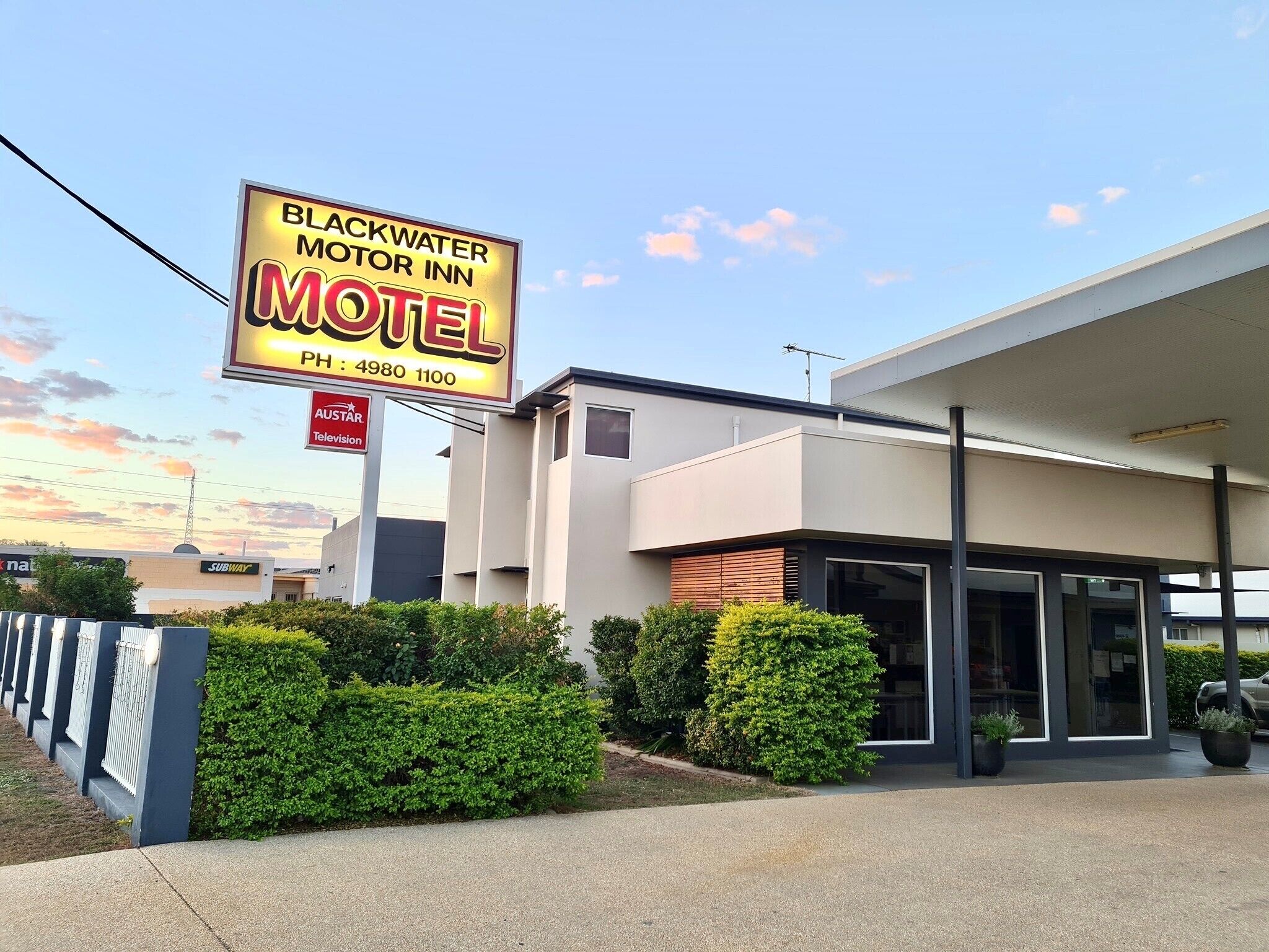 A motel with a modern building, a signboard, and a well-maintained hedge.