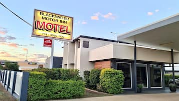 A motel with a modern building, a signboard, and a well-maintained hedge.