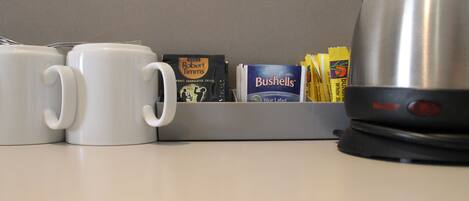 Una encimera de cocina con dos tazas blancas, una cafetera y varios productos de café, incluyendo un paquete de café Robert Timms y una caja de café Bushells.