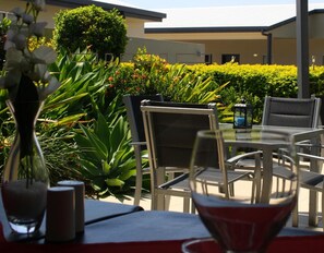 An outdoor dining area with metal chairs and tables, surrounded by lush greenery and a building in the background. - Blackwater Motor Inn (Blackwater)