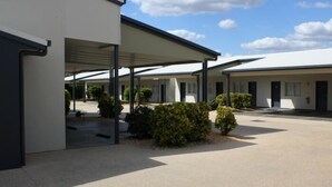 Une rangée de bâtiments de style motel, dotés d’un parking couvert et de petits arbustes devant.