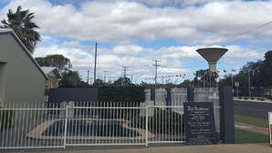 Une entrée fermée par un portail, avec une enseigne indiquant le restaurant Jags, une fontaine et un ciel dégagé.