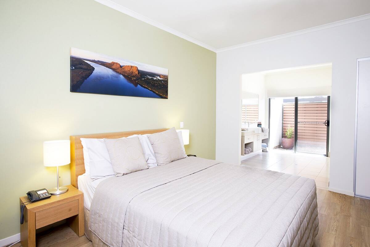 Une chambre d’hôtel avec un grand lit, des lampes de chevet, un tableau au mur et une vue sur l’extérieur grâce à une porte vitrée.