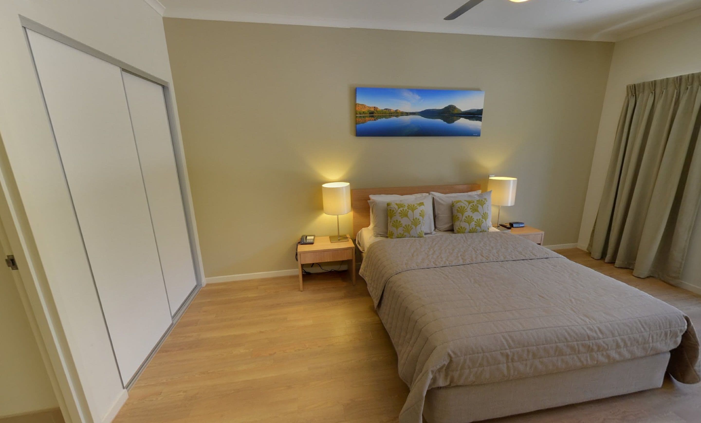 A hotel room with a bed, two bedside tables with lamps, a painting on the wall, and a door.