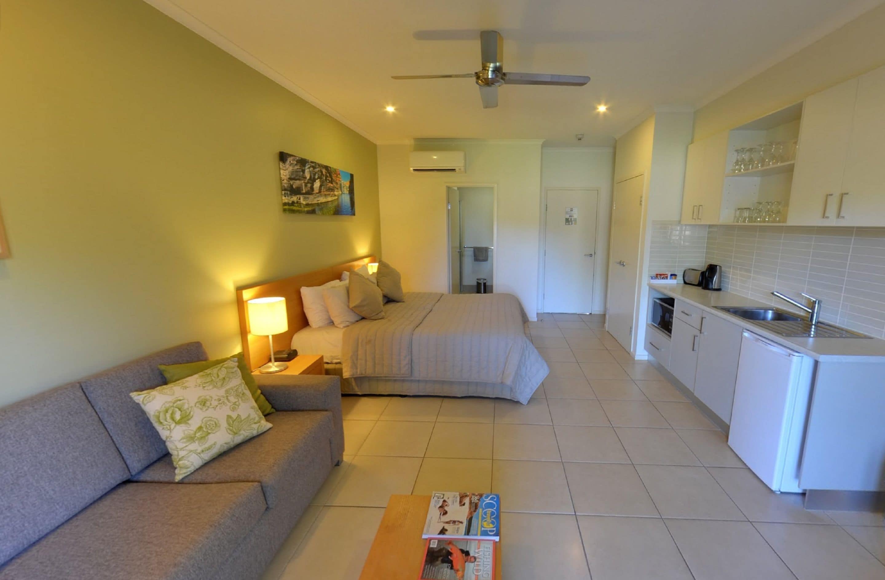 Een kleine hotelkamer met een bed, een slaapbank, een salontafel en een kitchenette.