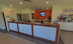 Un espace d’accueil avec un comptoir en bois, des certificats encadrés accrochés au mur, un téléviseur et un présentoir rempli de brochures.