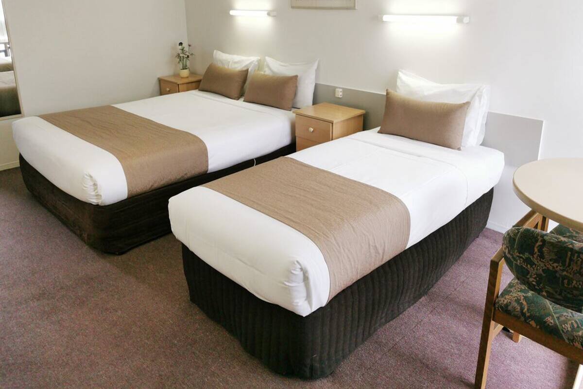 A hotel room with two beds, a small table, and a chair.