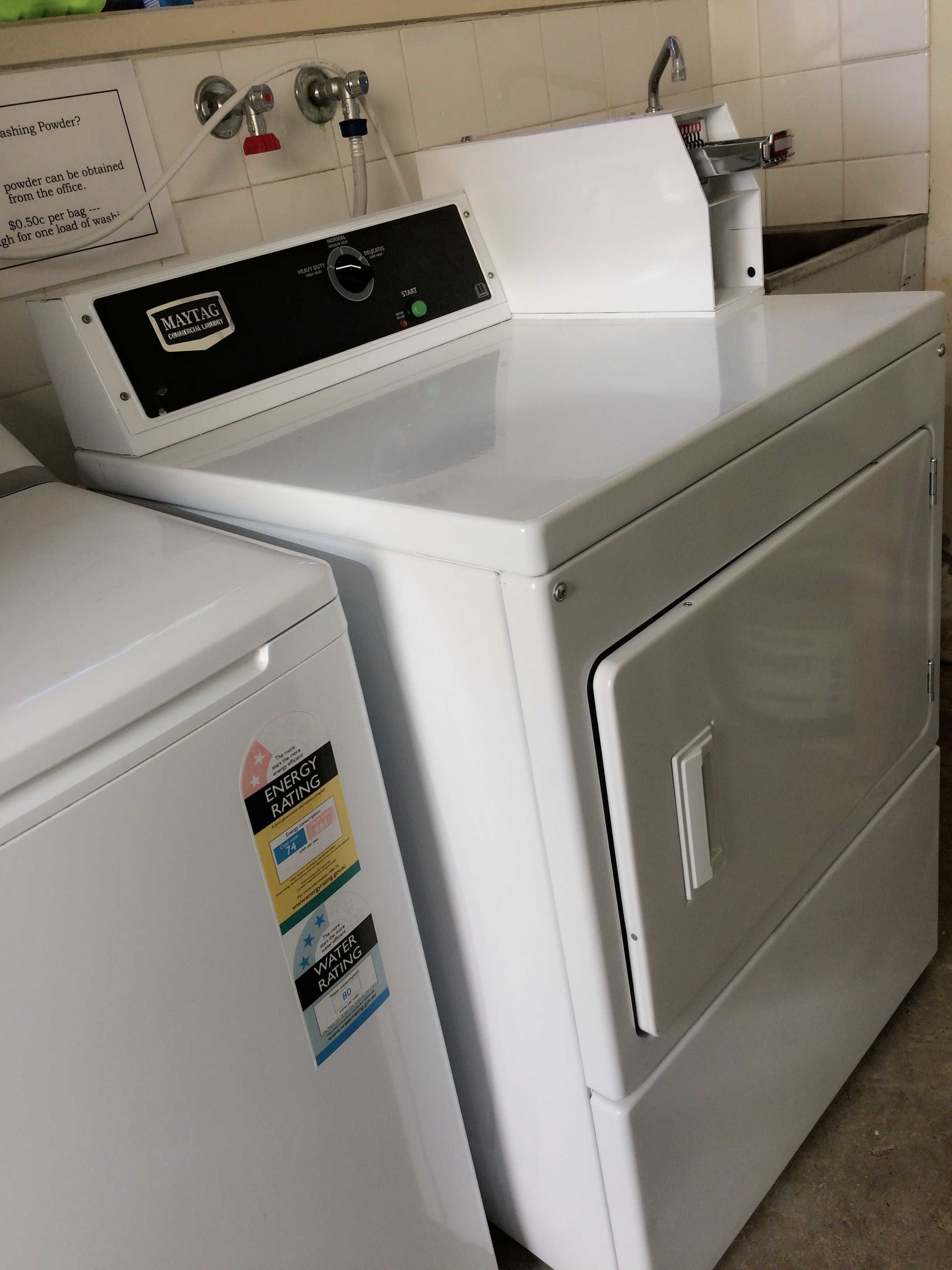 A front-loading white washer and dryer unit with a control panel, a water inlet, and a drain hose.