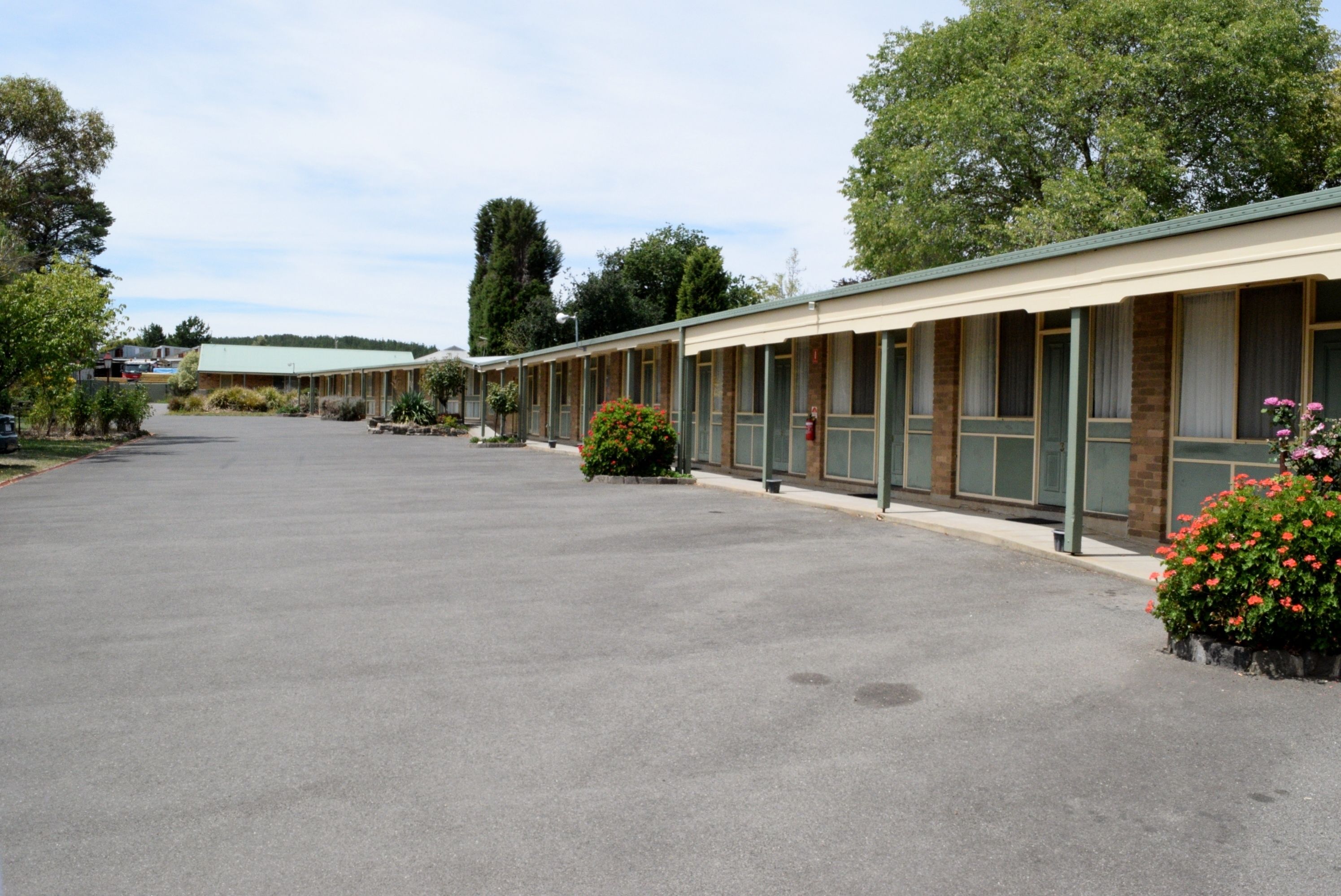 A row of motel rooms with a parking lot in front.