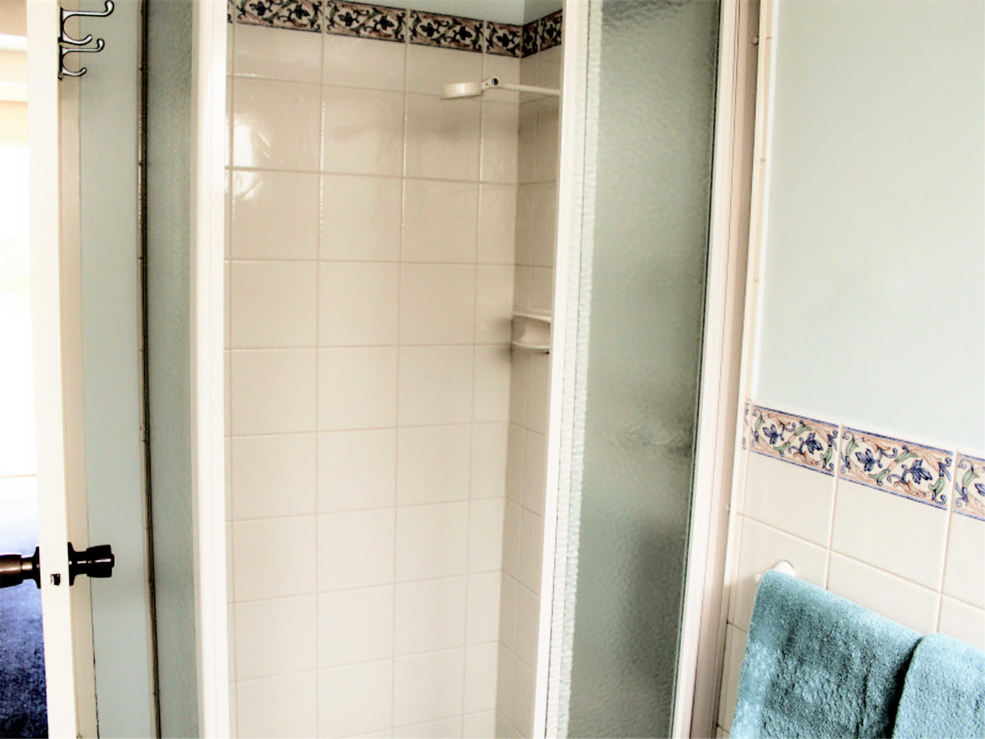 A bathroom with white tiles, a shower, and a towel rack.
