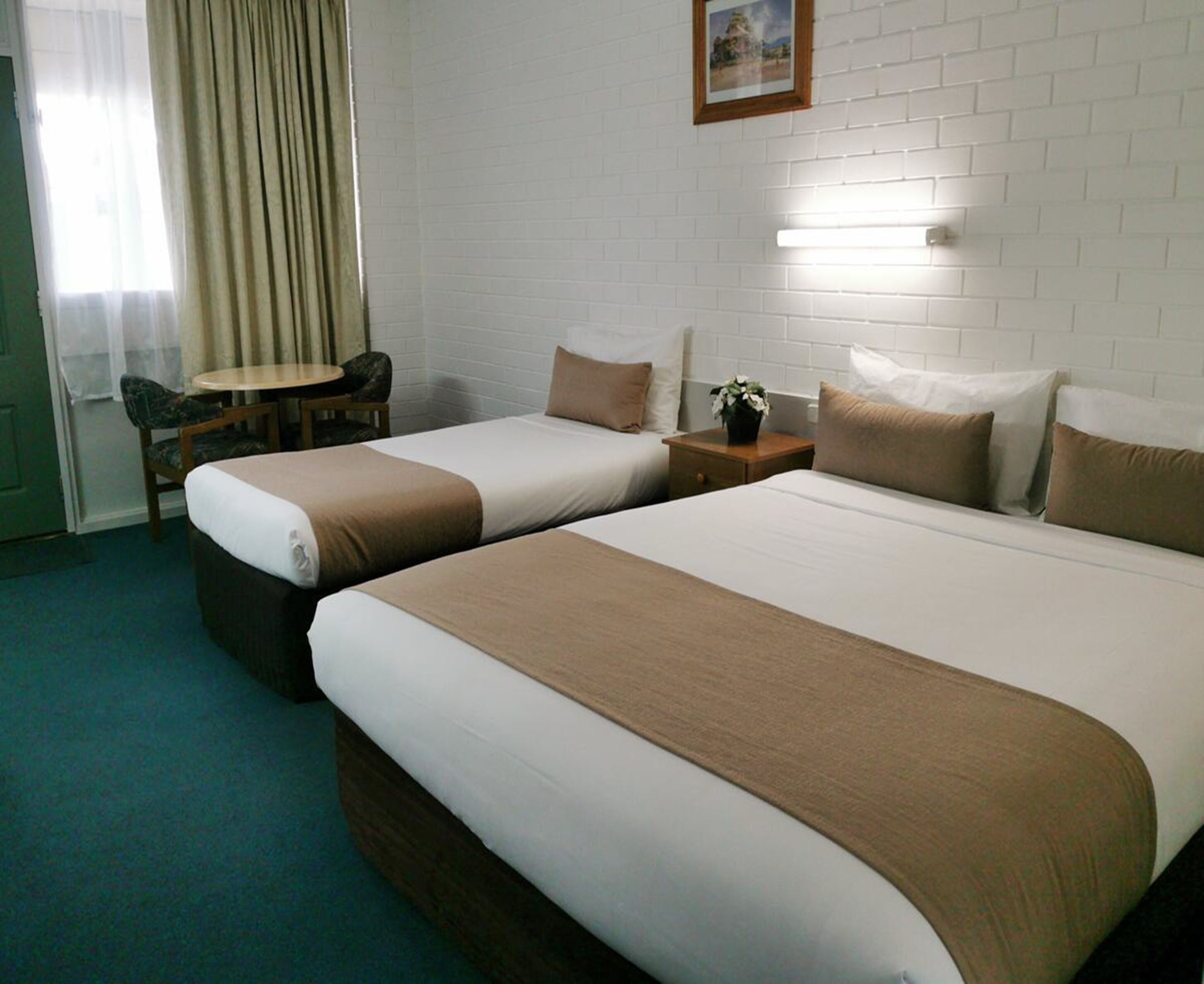 Een hotelkamer met twee bedden, een tafeltje, een stoel en een potplant.