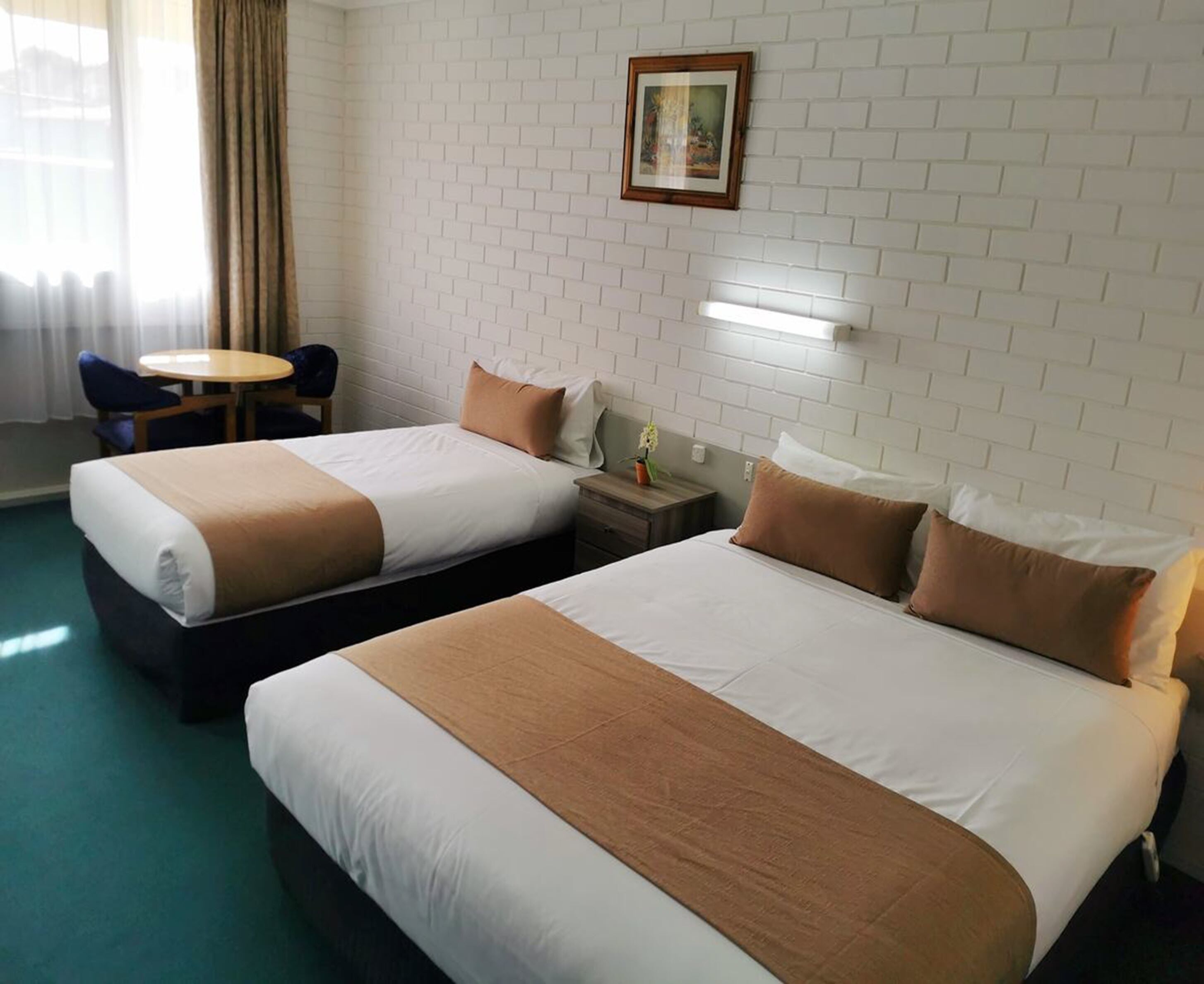 Una camera d'albergo con due letti, un tavolino, una sedia e un quadro appeso al muro.
