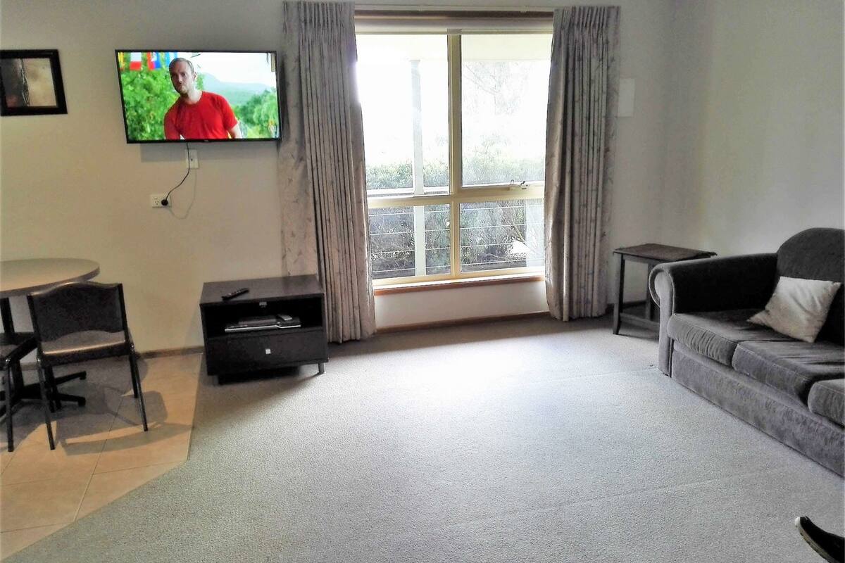 A living room with a TV, a sofa, a chair, a small table, and a window with curtains.