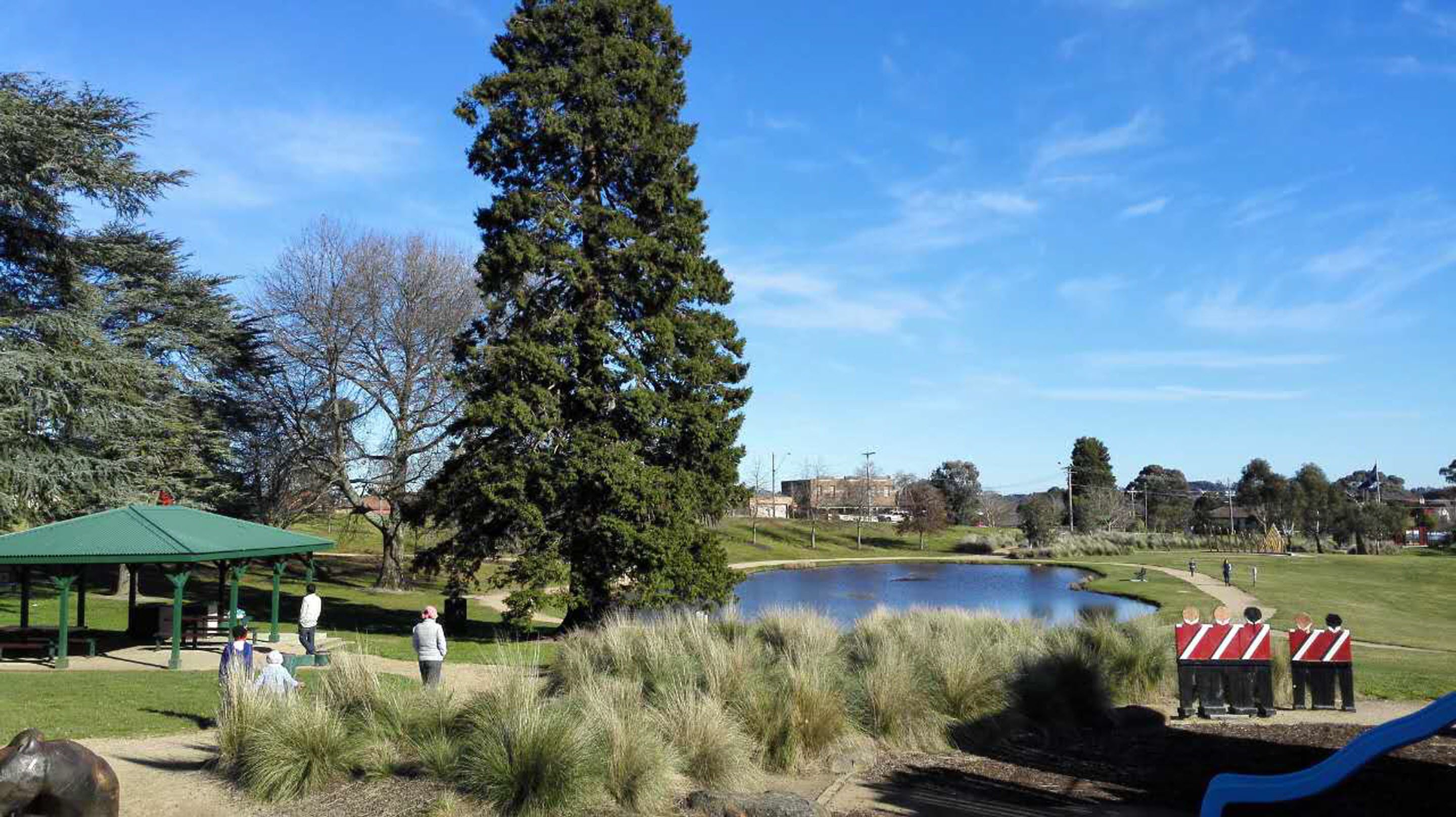 Ein Park mit einem großen Teich, Picknicktischen und einem hohen Baum.