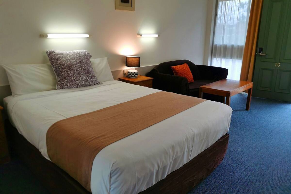 A hotel room with a bed, bedside tables, a desk, a chair, and a door.