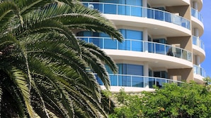A multi-story hotel with balconies, a palm tree in the foreground, and a clear blue sky. - Sails Luxury Apartments, Forster (Forster)