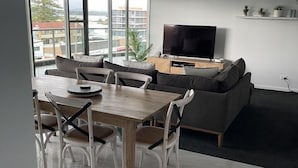 A modern living room with a dining area, large windows, and a flat-screen TV. - Sails Luxury Apartments, Forster (Forster)