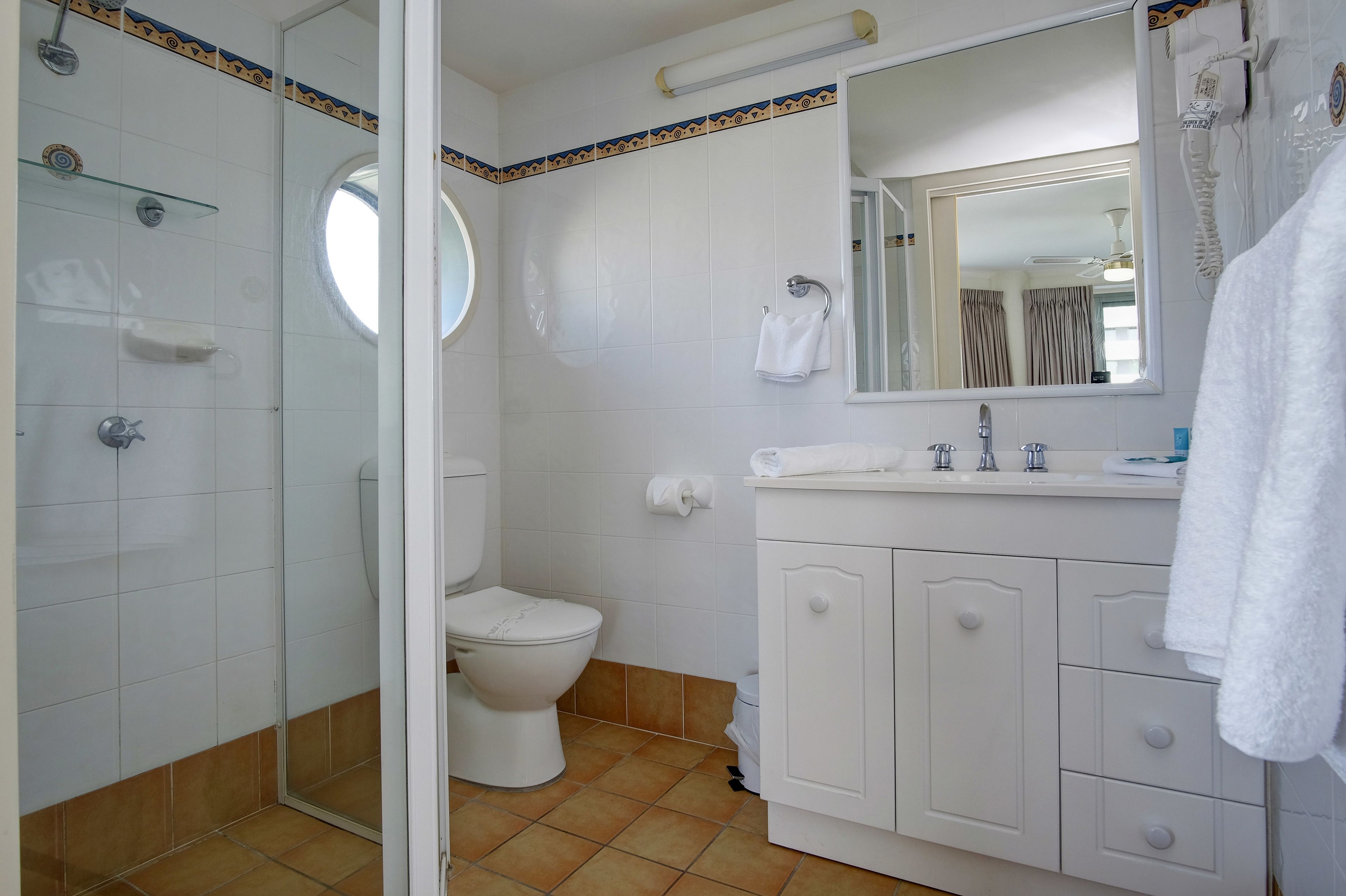 A bathroom with a shower, toilet, and vanity with a mirror.