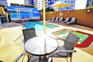 Zona de piscina con un mural, sillones de descanso y una mesa.