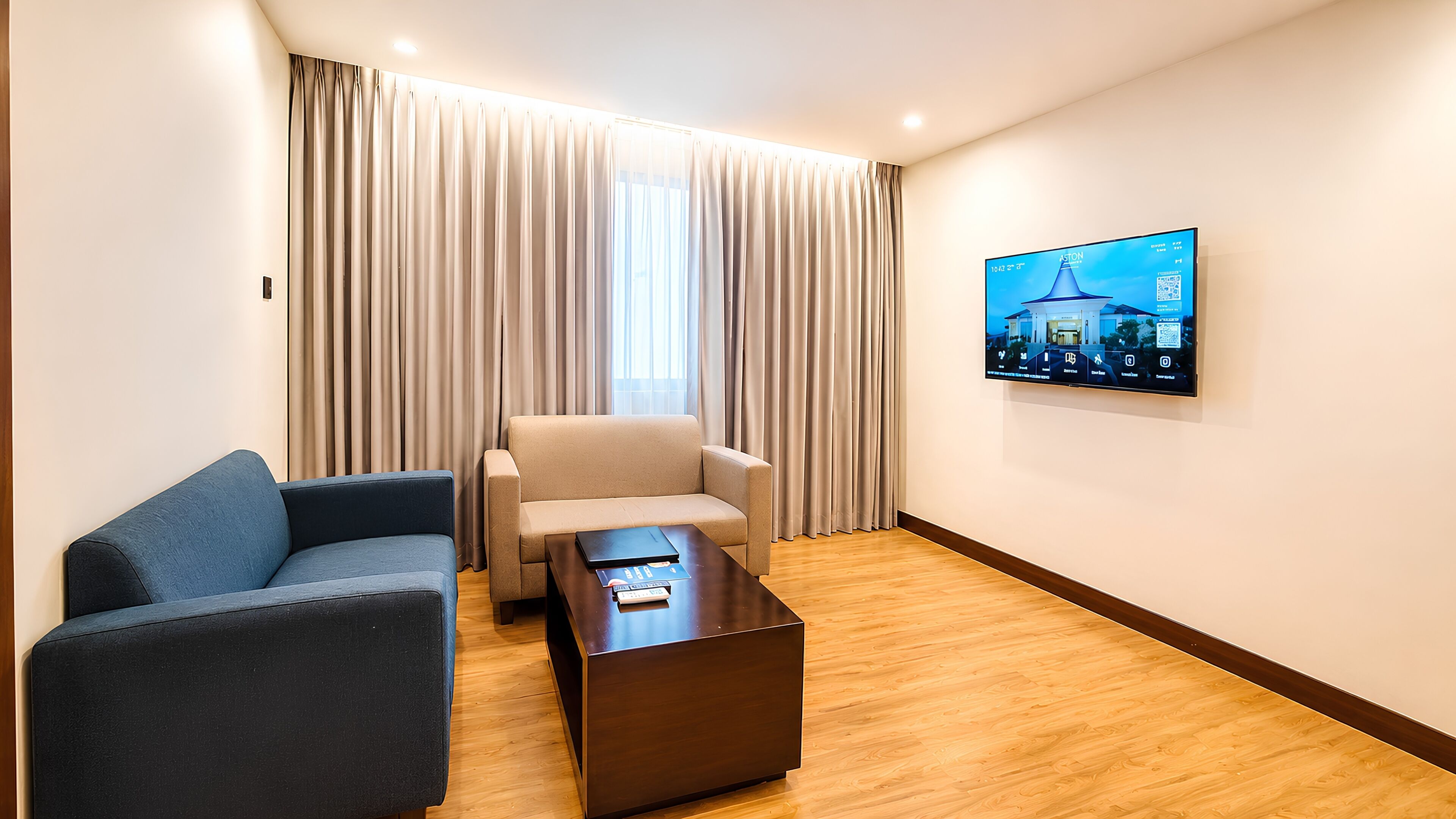 Habitación de hotel con sofá, sillón, mesa de centro y televisor en la pared.