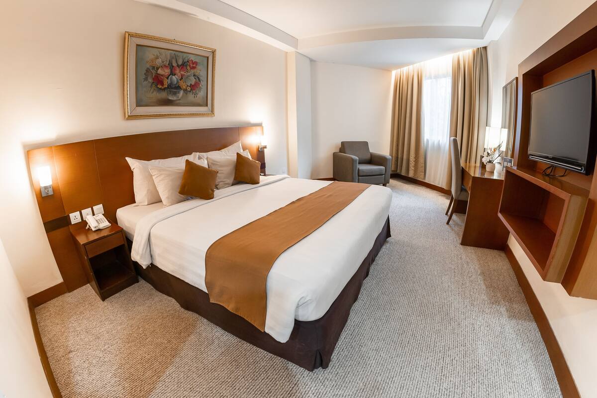A hotel room with a large bed, a bedside table with a phone, a chair, a TV, and a painting on the wall.
