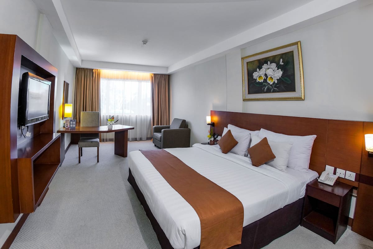 A hotel room with a large bed, a desk, a chair, a television, and a painting on the wall.