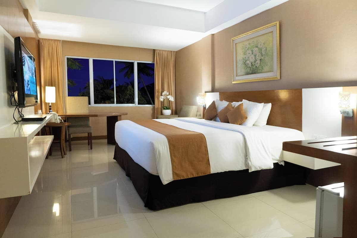 A hotel room with a large bed, a desk, a chair, a TV, and a window with curtains.