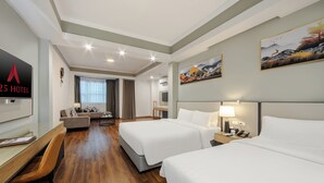 A hotel room with two beds, a desk, a sofa, and a TV.