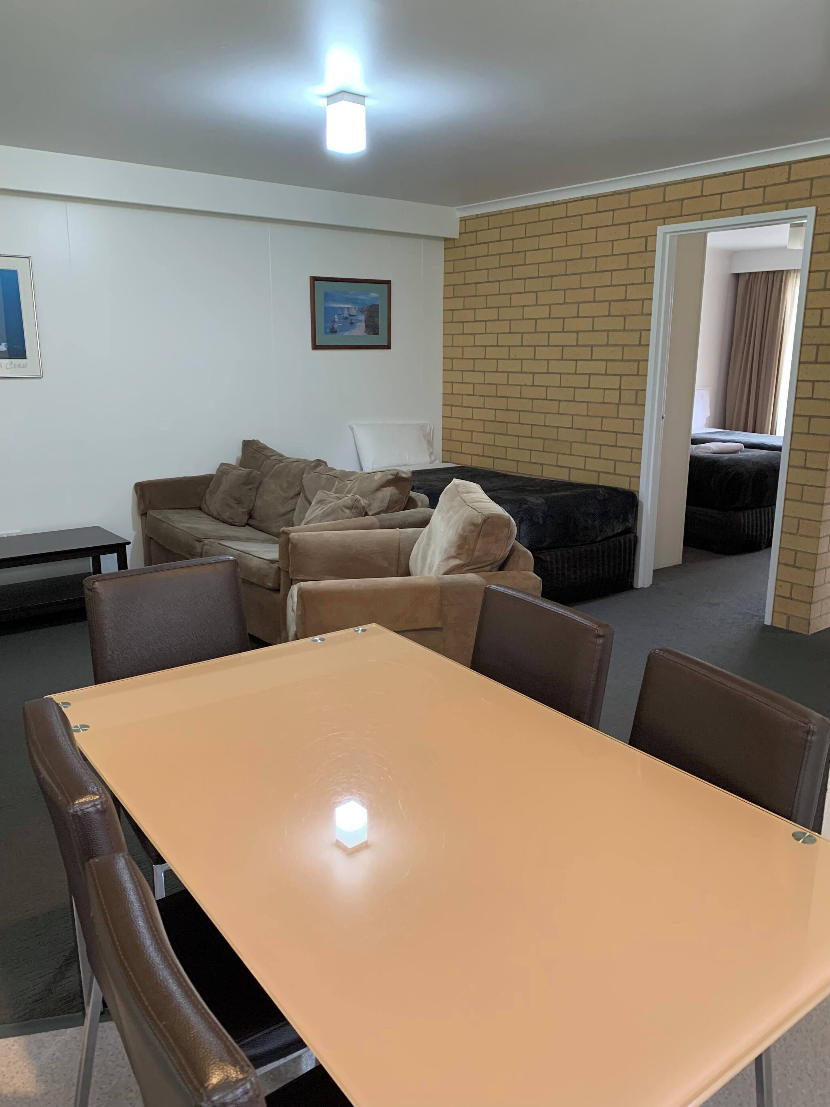 A room with a table and chairs, a sofa, a framed picture on the wall, and a brick wall.