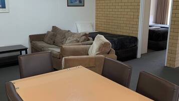 A room with a table and chairs, a sofa, a framed picture on the wall, and a brick wall.