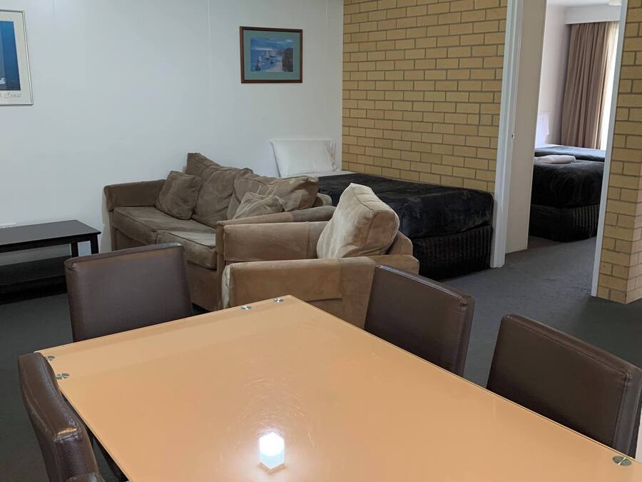 A room with a table and chairs, a sofa, a framed picture on the wall, and a brick wall.