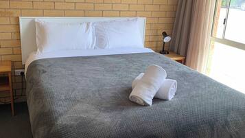 A hotel room with a brick wall, a large bed with white pillows, a grey blanket, and a rolled towel on the bed.