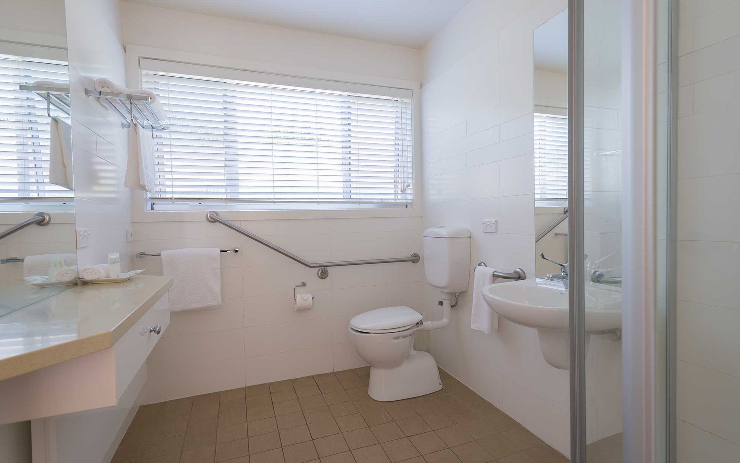 Un baño con inodoro, lavamanos y ventana con persianas.