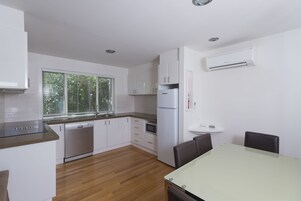 Una cocina moderna con armarios blancos, lavavajillas, refrigerador y una ventana con persianas.