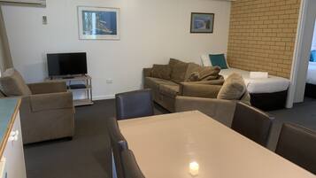 A compact living space with a sofa set, a TV, a small table, and a bed.