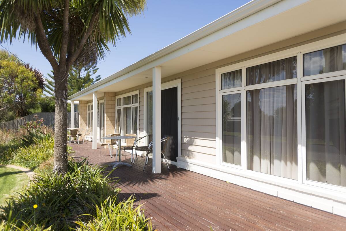 A covered outdoor area with a wooden deck, a palm tree, and a seating area with chairs and a table.