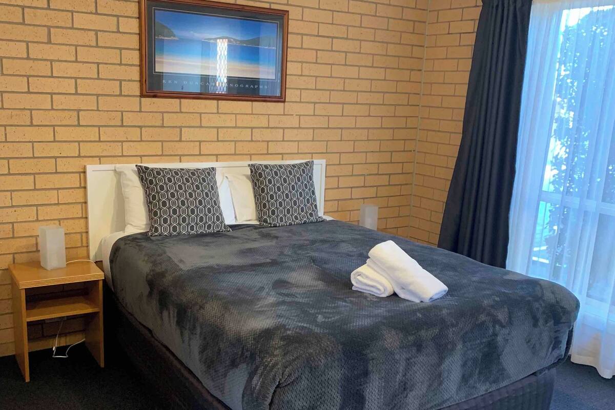 A hotel room with a large bed, a nightstand, a ceiling fan, and a window with curtains.