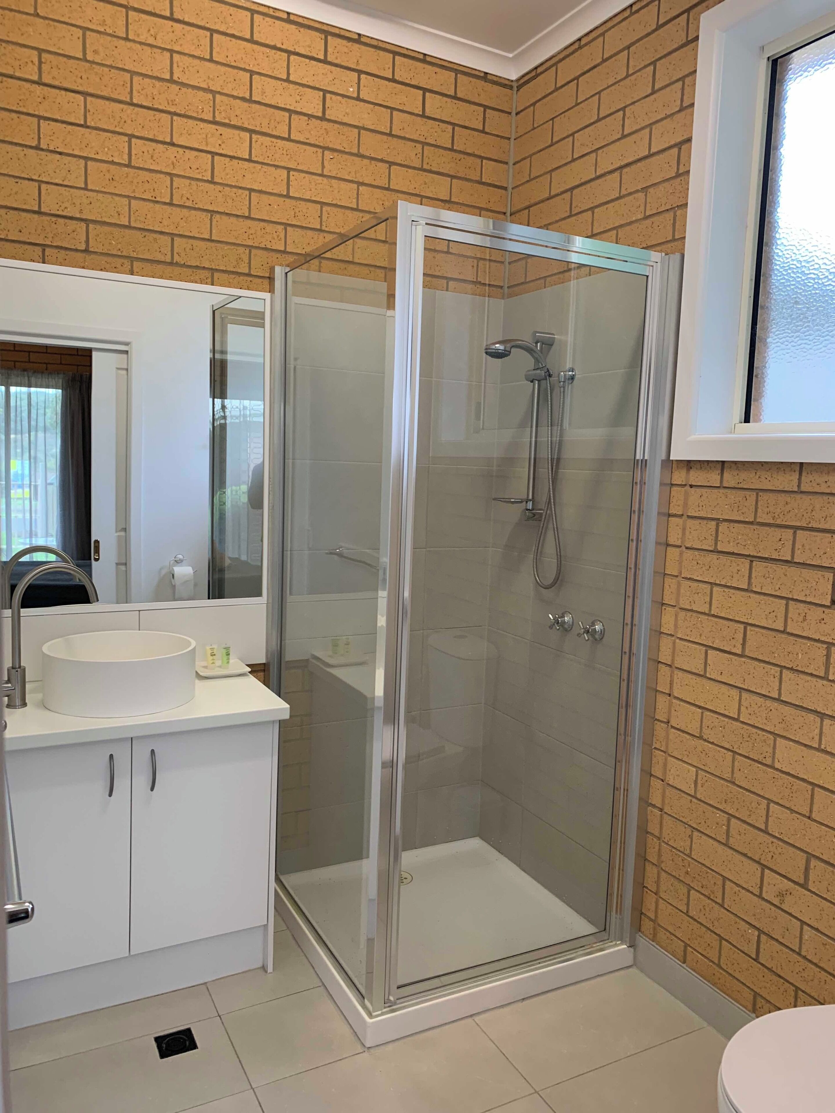A bathroom with a glass-enclosed shower, a sink with a mirror, and a window.