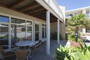 An outdoor patio area with a table and chairs, surrounded by glass doors and windows, and a small garden with plants. - Port Campbell Parkview Motel & Apartments (Port Campbell)