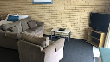 Ein Hotelzimmer mit einer Ziegelwand, einem gerahmten Bild, einer Couch, einem kleinen Tisch mit einem Tablet und einem Fernseher auf einem Holzboden.